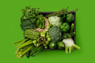 Various fresh green vegetables in wooden box on green background