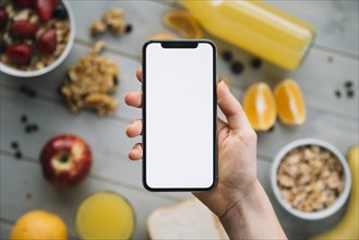 Person holding smartphone with blank screen table with fruits