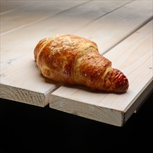 Fresh crisp croissant with powdered sugar on the corner of wooden table