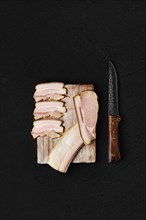 Assortment of slices of smoked pork bacon and lard on wooden cutting board