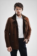 Brutal handsome unshaven man with beard and moustache in sheepskin coat with fur collar