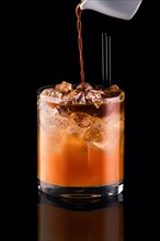 Pouring espresso in glass with tonic and ice isolated on black background