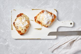 Top view of crispy croissant with caramel and peanut shavings on white serving board on marble background