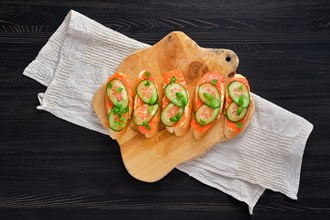 Top view of sandwich with salmon on wooden plate on dark wooden table