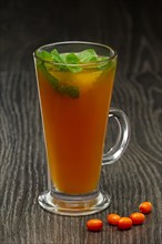 Glass of hot tea with sea buckthorn and mint on wooden table soft focus photo