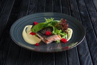 Fried piece of salmon with creamy sauce and green salad leaves decorated with caviar