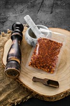 Wooden cross section with chili flakes in plastic package and stone mortar and mill