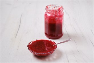 Jar and saucer with cherry jam on white wooden background