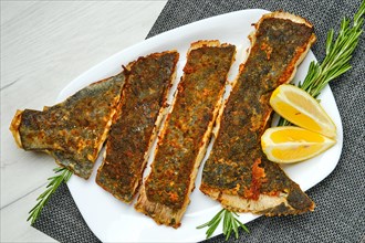 Top view of fried flounder in breading cut on pieces served with lemon on white wooden table