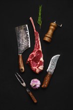 Overhead composition with raw beef cowboy steak and butcher tools over back background