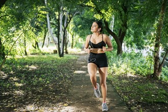 Sporty young woman running in a park. A girl running in a park while listening to music. Lifestyle of beautiful girl running in a park surrounded by trees. Healthy lifestyle concept