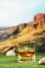 Facetted glass of peat whiskey on green moss
