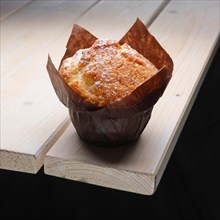Fresh muffin with powdered sugar in paper wrapper on the corner of wooden table