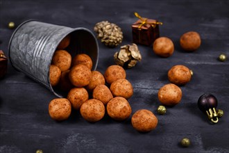 Traditional German Christmas sweets called Marzipankartoffeln. Round ball shaped almond paste pieces covered in cinnamon and cocoa powder spilling out of iron cup on dark background