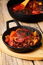 Closeup view of cast iron skillet with ossobuco on wooden table
