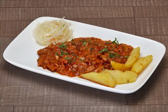 Beef goulash with potato wedges and pickled cabbage on wooden table