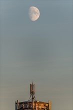 Moon over telecommunication antenna on water tower. France
