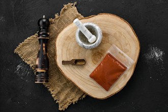 Wooden cross section with chilli pepper in plastic package and stone mortar and mill