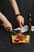 Cutting juicy steak on wooden cutting board over black background