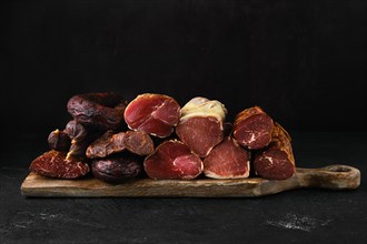 Assortment of dry-cured beef meat and sausages on dark background