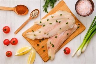 Top view of raw fresh haddock fillet on wooden cutting board with spice and herbs