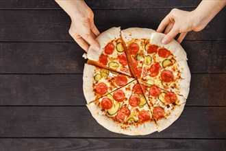Top view of two hands taking slice of pizza pepperoni from plate
