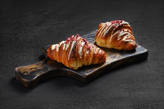 Crispy croissant with raspberry on rustic wooden serving board