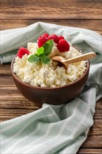 Fresh cottage cheese with raspberries and wooden spoon in clayware on wooden table