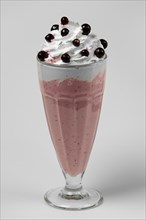 Milkshake black currant summer cocktail in tall facetted glass on gray background