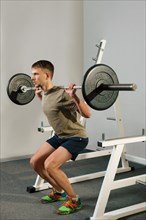 Athletic man doing squats exercise with dumbbell. Strong man doing barbell squats