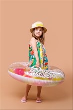 Cute child in sundress and straw hat with swimming ring playing in studio