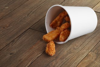 Cardboard container with fried chicken wings laying on wooden floor
