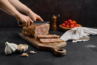 Female hand with knife cut boiled beef tongue roll on wooden cutting board
