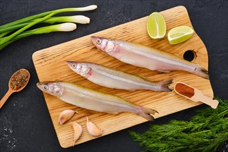 Top view of raw fresh smelt fish on wooden cutting board with spice and herbs