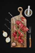 Top view of skewers with raw beef meat and spice on dark background