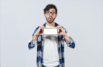 Surprised guy in glasses showing blank screen of smart phone. Amazed young man showing ad on cellphone. Surprised handsome man showing the horizontal screen of his cell phone