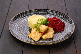 Fried hake in breading with mashed potato and roasted beetroot on dark wooden table