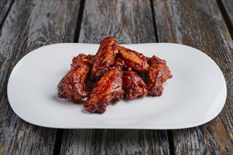 Tasty grilled chicken wings Buffalo on a white dish on wooden table