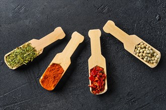 Four small wooden spoons with spice on black concrete background