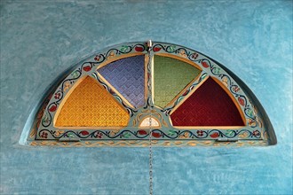 Decorated window with coloured glass in turquoise wall