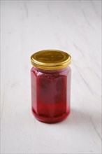 Whole closed jar of cherry jam on white wooden background
