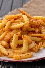 Fried crinkle cut french fries on dark wooden table