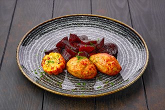 Plate with fried pork cutlet with roasted beetroot slices and grilled maize on dark wooden table