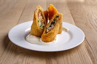 Deep-fried pancakes stuffed with ham and covered with melted cheese on wooden table