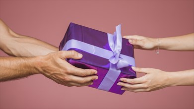 Close up couple holding wrapped purple gift box against colored background