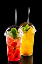 Two take away glasses with strawberry and orange lemonade isolated on black background
