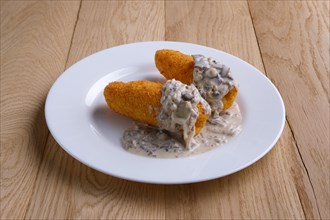 Potato cutlet in breading stuffed with ham served with mushroom sauce on wooden table