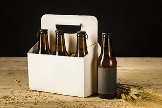 Beer bottle carton box and ears of wheat on wooden surface
