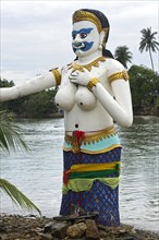 Bare-breasted mermaid statue with masculine features stands on the shore