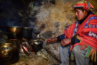 Quechua Indian in traditional dress cooking at the fireplace of his hut